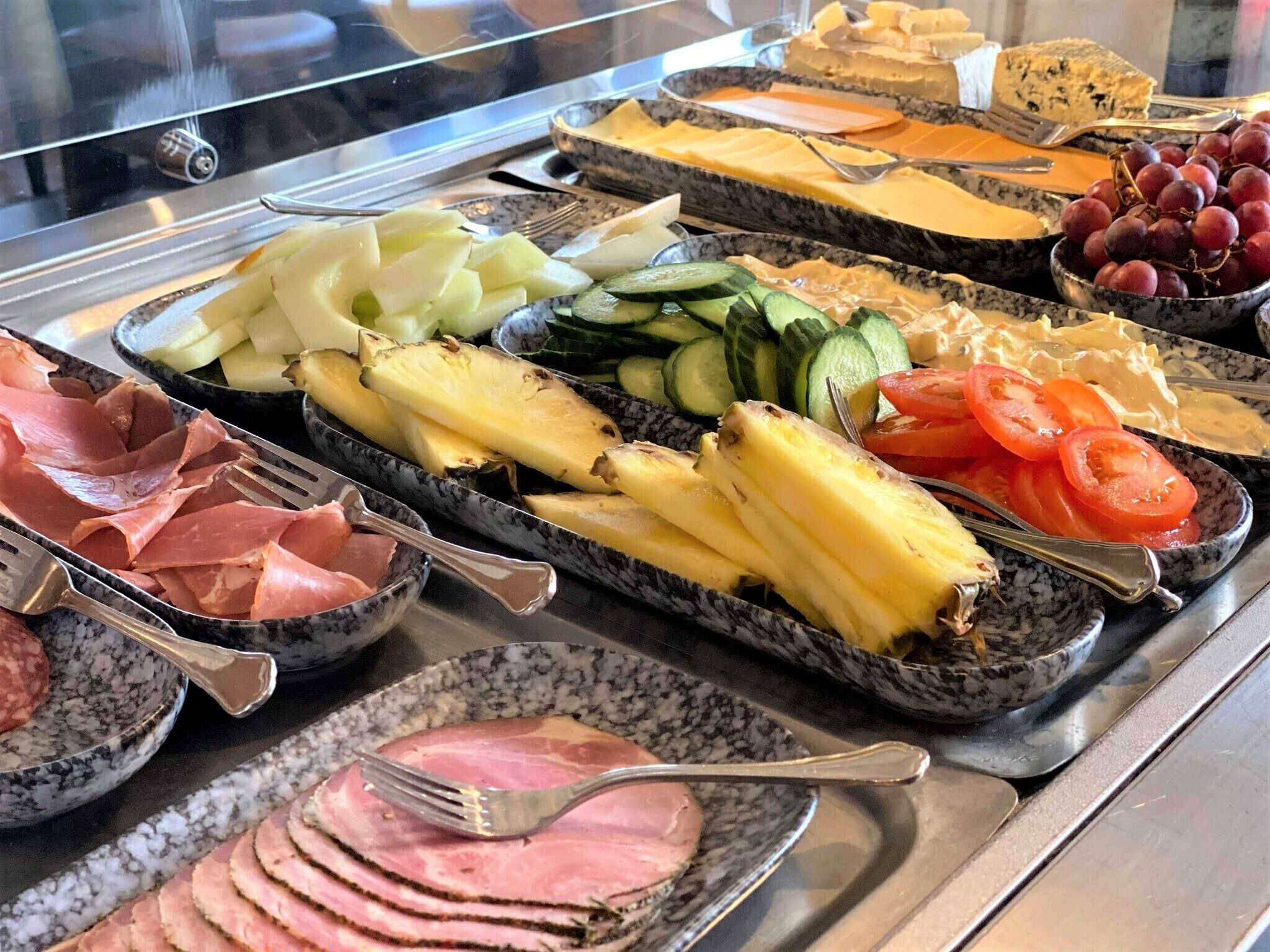 A buffet with various food items including meats, cheeses, fruits, and vegetables.