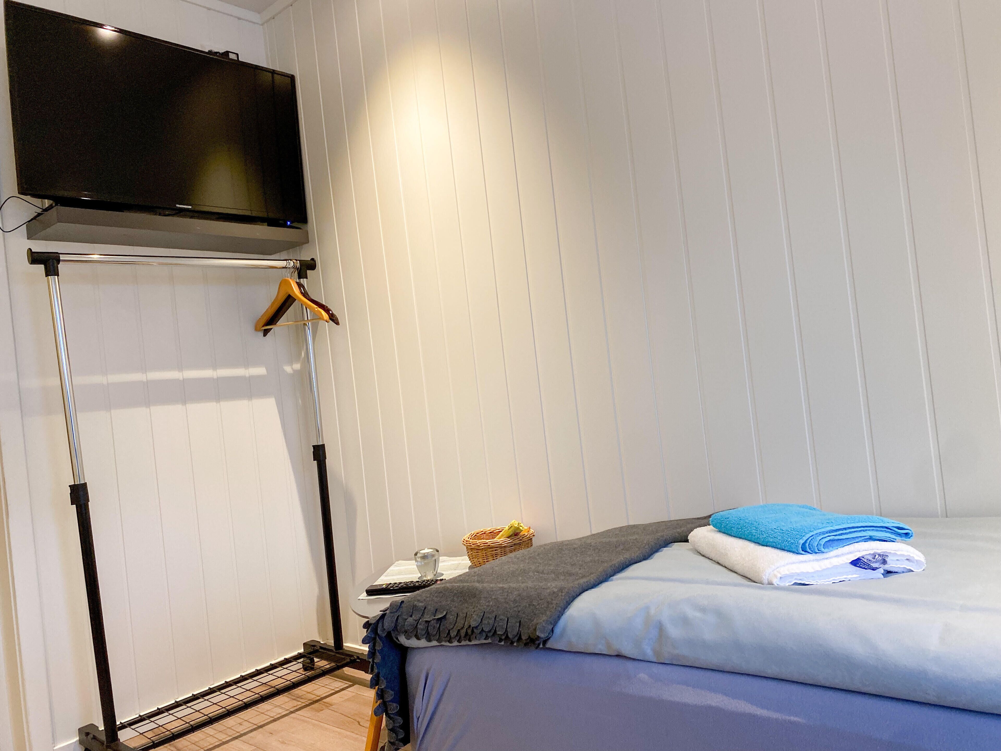 A hotel room with a bed, a TV mounted on the wall, a drying rack, and a small table with a basket and a glass.