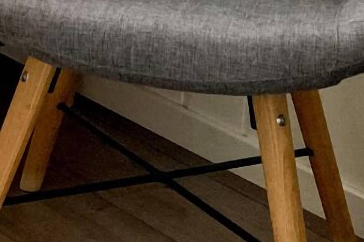 Een grijze fauteuil met houten poten en een gebogen rugleuning.