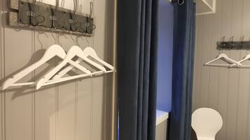 Ein Zimmer mit einer Holzwand, einem Fenster mit blauen Vorhängen, einem weißen Stuhl und einem Kleiderständer mit weißen Kleiderbügeln.
