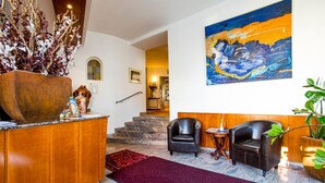 A lobby with a reception desk, two leather chairs, a large abstract painting, a staircase, and a potted plant. - Hotel Wegener (Mannheim)