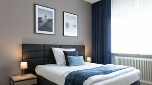 A modern hotel bedroom with a large bed, two bedside tables, a headboard, and two framed pictures on the wall. - Hotel Wegener (Mannheim)