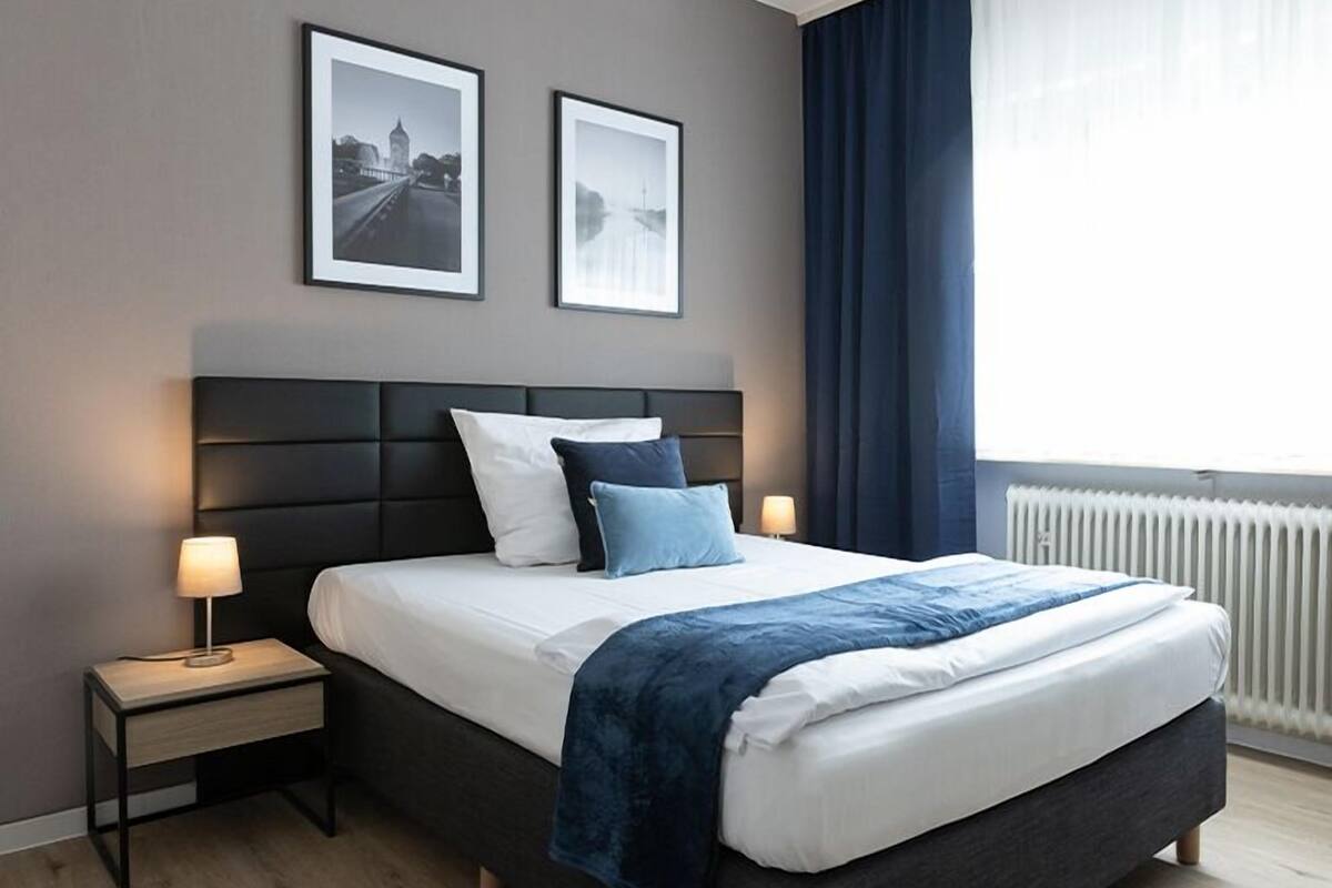 Un dormitorio moderno de hotel con una cama grande, dos mesitas de noche, un cabecero y dos cuadros enmarcados en la pared.