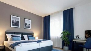 A hotel room with a bed, a desk, a chair, a television, and a potted plant. - Hotel Wegener (Mannheim)