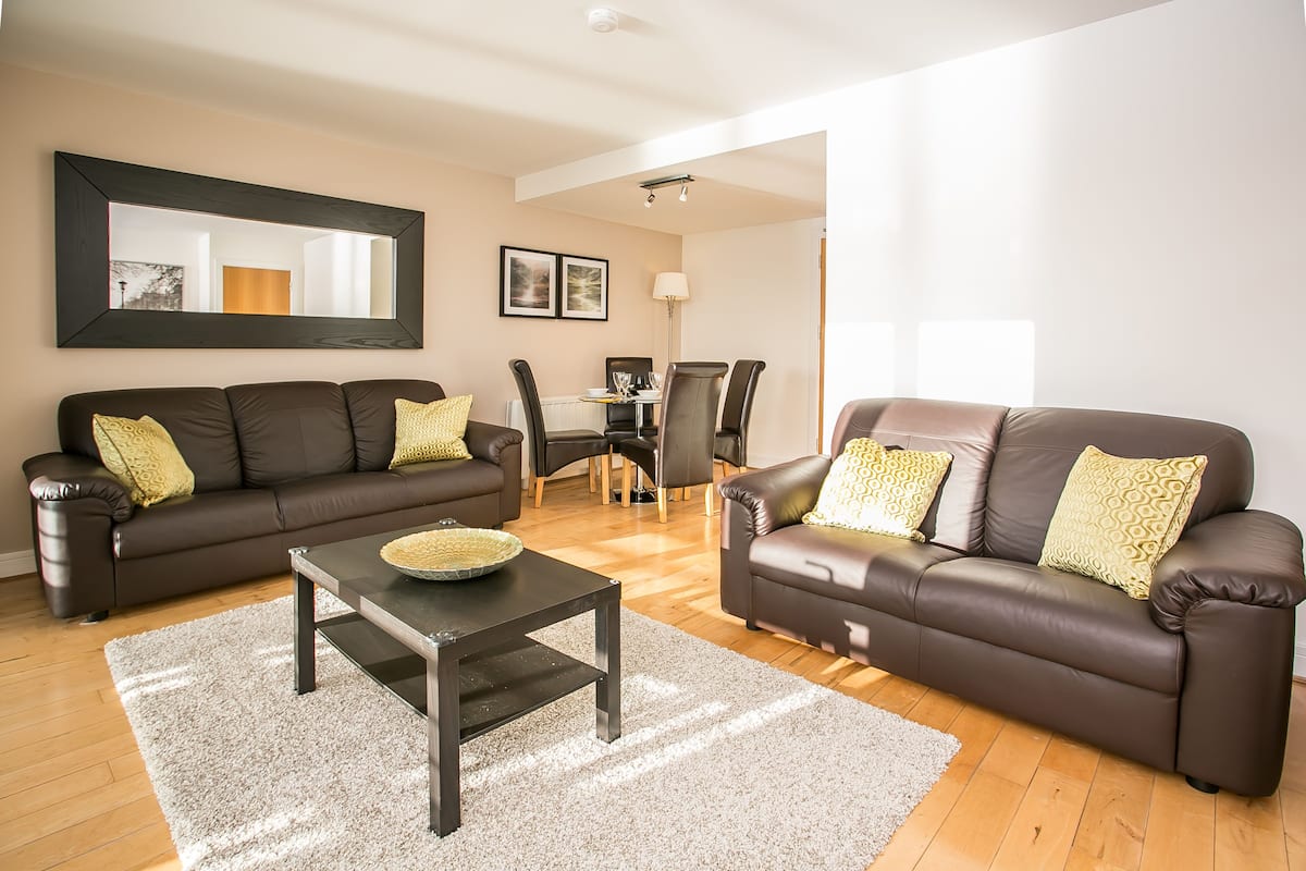 A living room with two brown leather sofas, a glass coffee table, and a dining table with chairs.