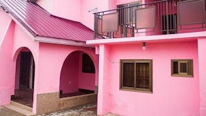A pink two-story house with a balcony, arched doorways, and a metal roof.