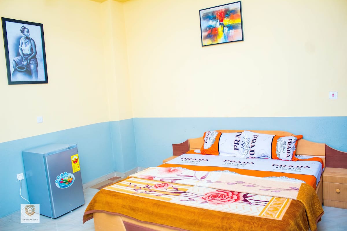 A hotel room with a bed, a refrigerator, and a wall with a framed picture.
