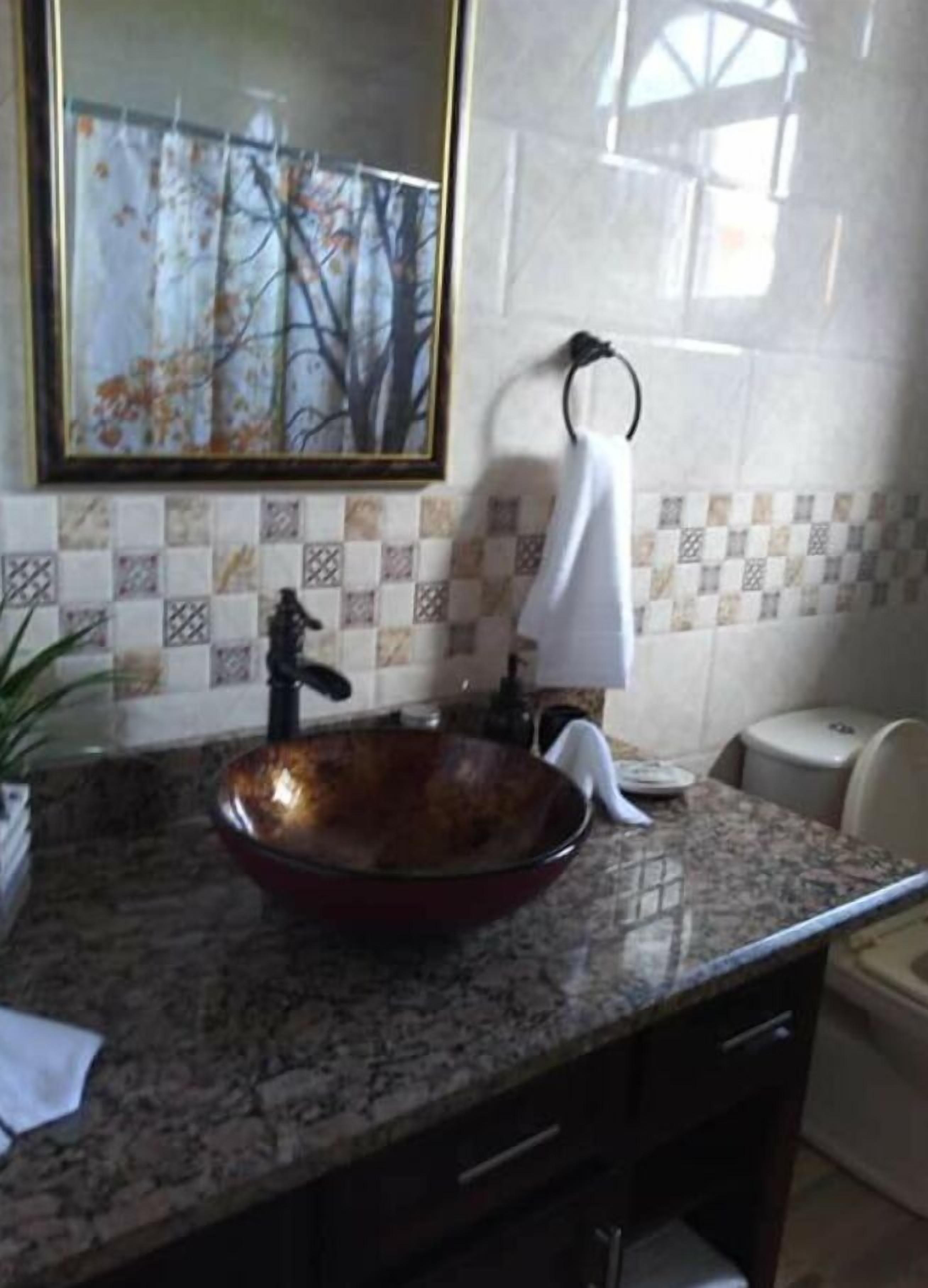 Een badkamer met een groot, rond, koperkleurig wastafel, een handdoekhouder en een betegelde spatwand met een geruit patroon.