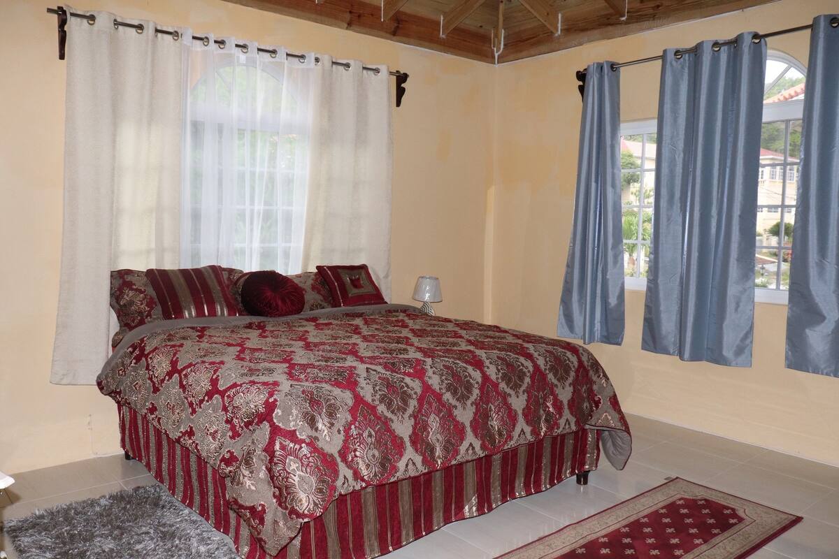 A bedroom with a large bed, a nightstand, and a window with curtains.