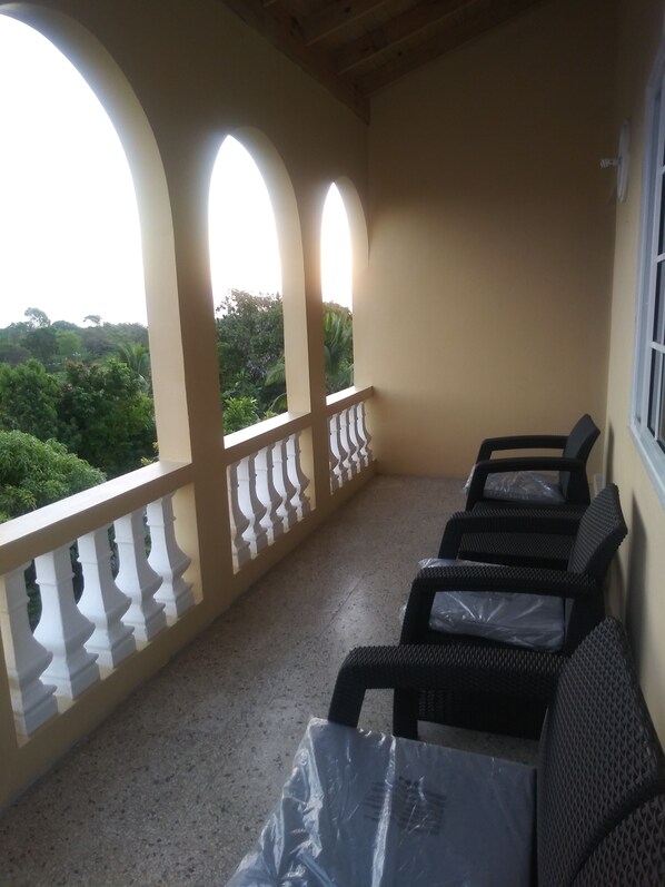 A balcony with a view of greenery, a railing, and a table with chairs.