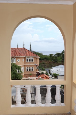 A balcony with white balustrades overlooking a building with a red-tiled roof and a view of the sea.