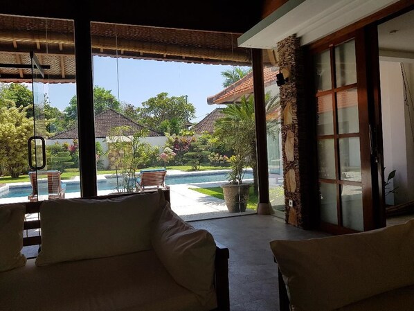 A room with a view of a swimming pool and garden, a large sliding glass door, and a cushioned seating area.