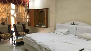 A bedroom with a large bed, a chair, a small table, and a mirror. - Iroomz Shanbhag Towers International (Hospet)
