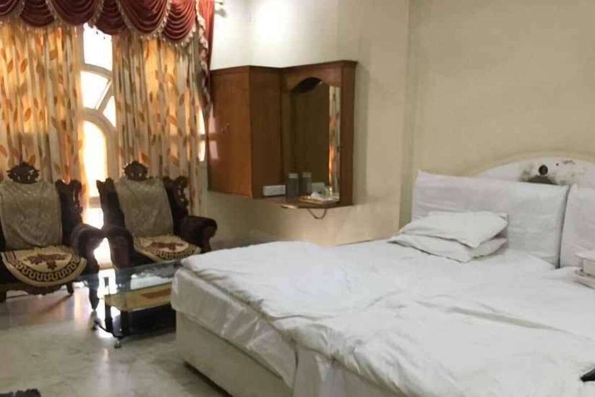 A bedroom with a large bed, a chair, a small table, and a mirror.