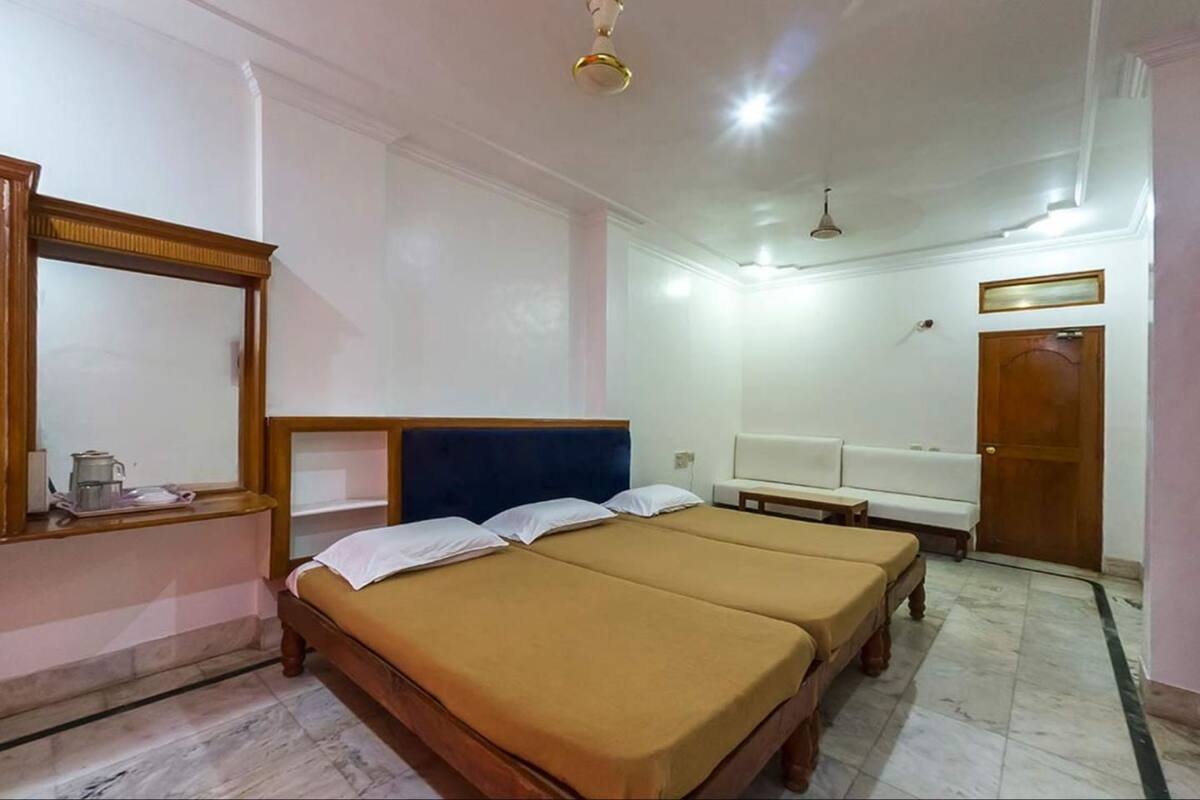 A hotel room with two beds, a wooden headboard, a mirror, a bedside table, a sofa, and a door.