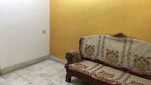 A corner room with a patterned sofa against a yellow wall and white tiled floor. - Iroomz Shanbhag Towers International (Hospet)