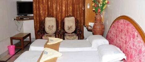 A hotel room with a bed, two chairs, a small table, a television, and a vase with flowers.