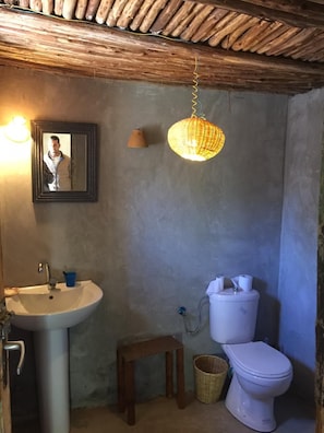 Un baño con un lavamanos blanco, un inodoro, una lámpara colgante y una fotografía enmarcada en la pared.