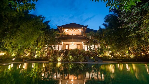 A traditional-style building with a reflection in the pool, surrounded by lush greenery. - Large Groups,9 BDR,Close To Beach,Great Inclusions (Canggu)