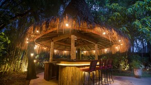 An outdoor bar area with a thatched roof, wooden bar counter, and several bar stools. - Large Groups,9 BDR,Close To Beach,Great Inclusions (Canggu)