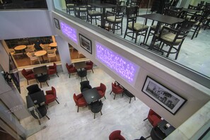 Un hall d’hôtel doté de plusieurs espaces aménagés avec des sièges, notamment des tables et des chaises, et d’une rambarde en verre donnant sur le niveau inférieur.