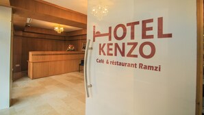 A reception area with a wooden reception desk and a chandelier. The sign reads "HOTEL KENZO Café & restaurant Ramzi". - Hotel Kenzo (Safi)