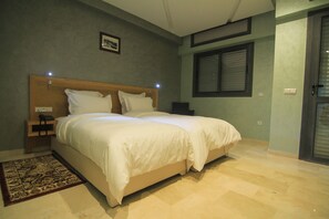 Une chambre à coucher avec un lit double, une table de chevet avec une lampe, une commode et une fenêtre avec des stores.