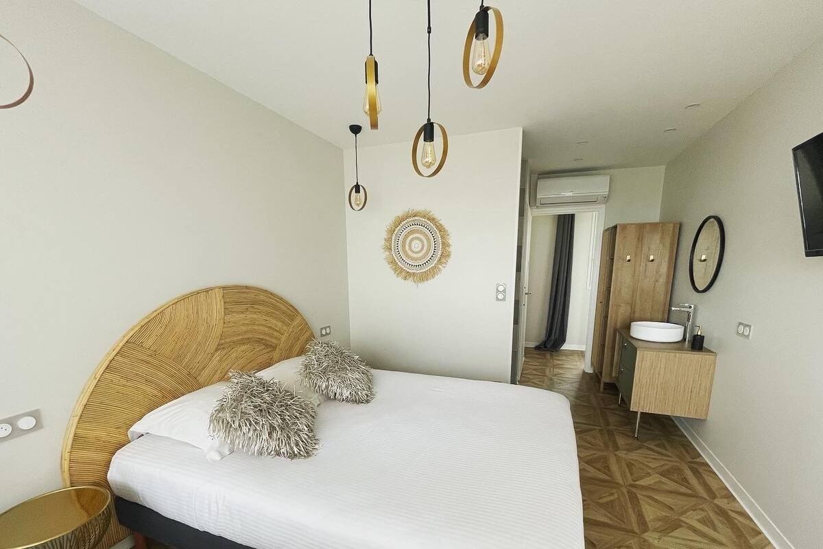 A modern hotel room with a large bed, a wooden headboard, a round wall decoration, a small bedside table, and a built-in wardrobe.