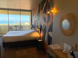 Habitación de hotel con una cama grande, un escritorio con cafetera, un espejo y vistas al mar.