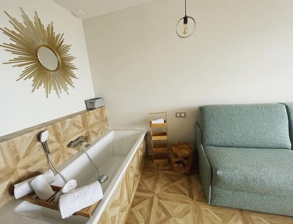 Un baño con bañera, tocador de madera, espejo y sofá verde.