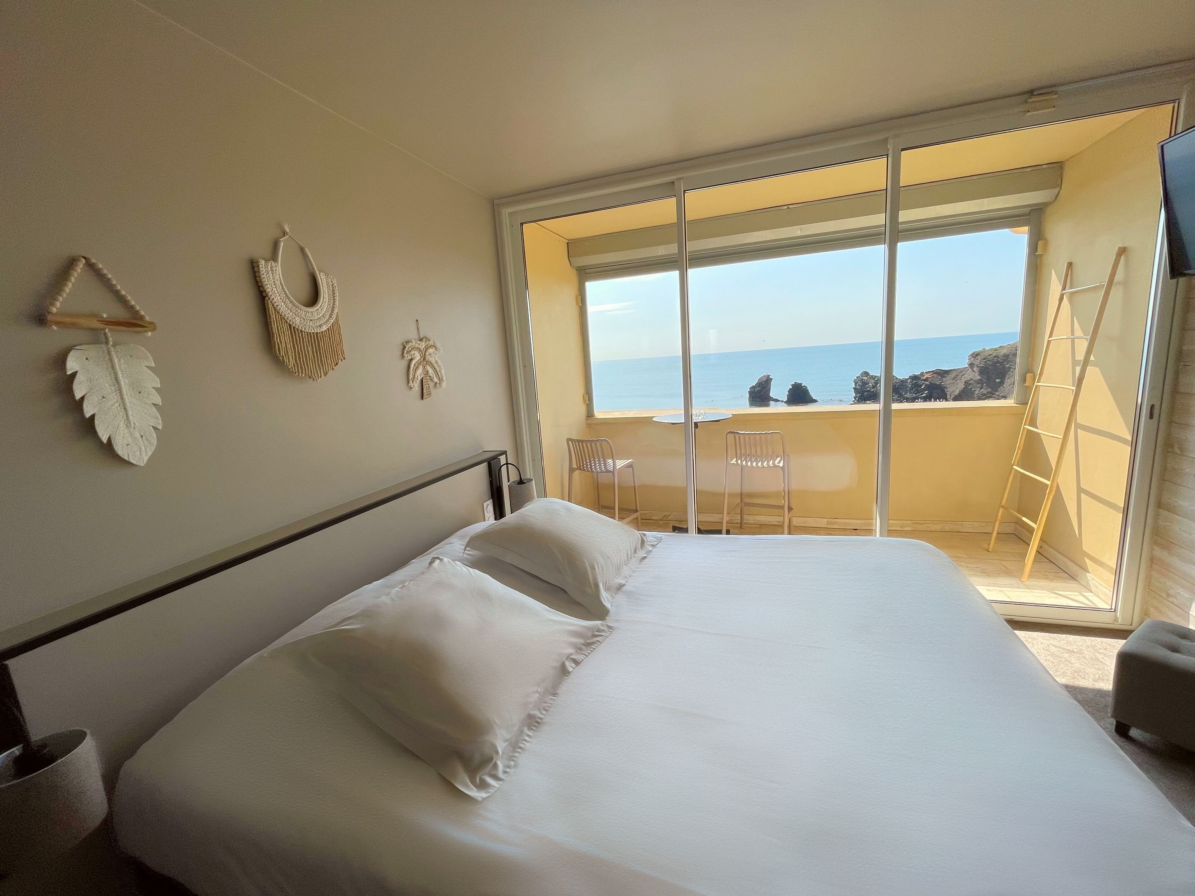 A bedroom with a large bed, a balcony with a view of the sea, and a chair.