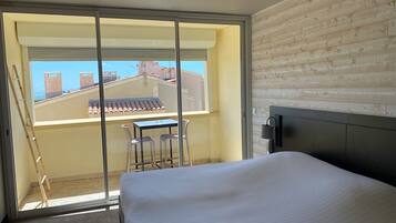 Un dormitorio con cama, una pequeña mesa con sillas, una ventana con vista a edificios y una pared de madera.