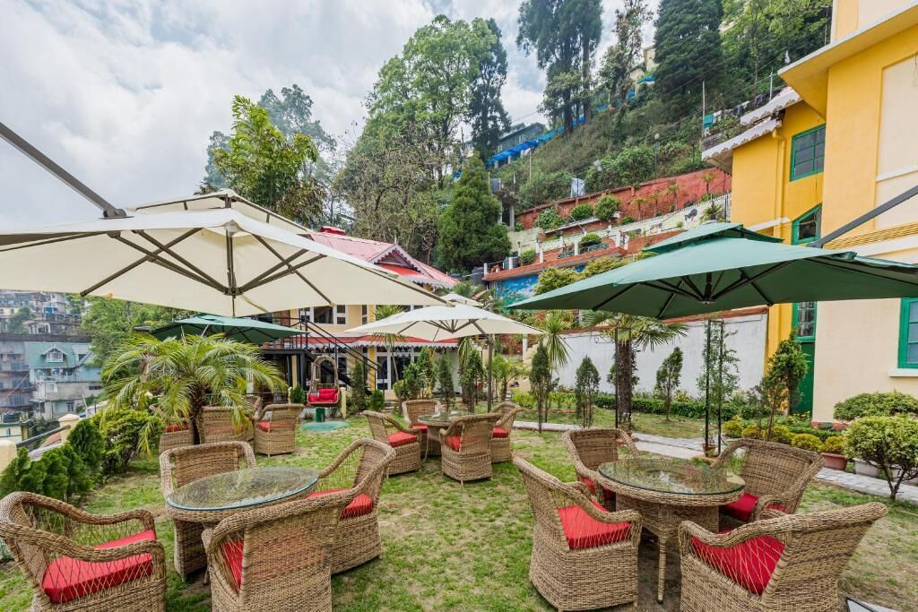 Un espace extérieur aménagé avec des meubles en osier et des parasols, entouré de verdure et de bâtiments.