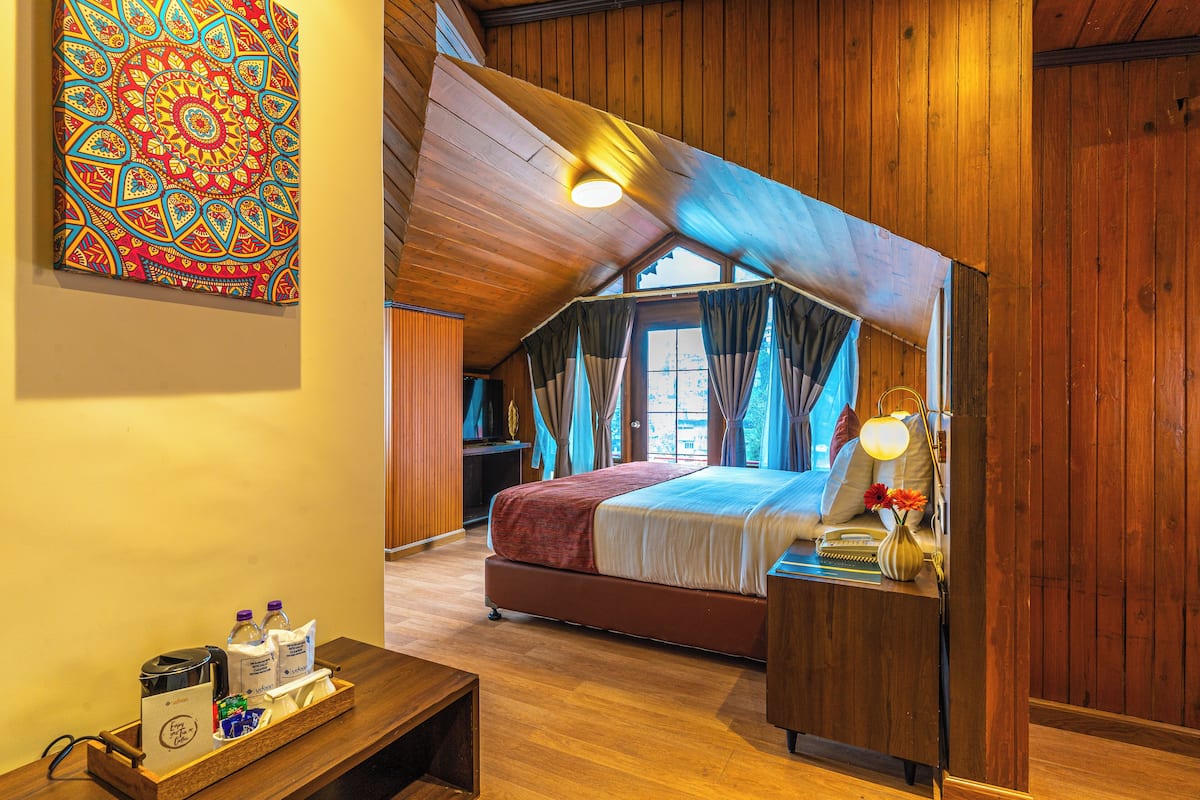 Een gezellig slaapkamer onder het dak met een houten plafond, een groot bed, een nachtkastje met lamp en een kleurrijk wandtapijt.