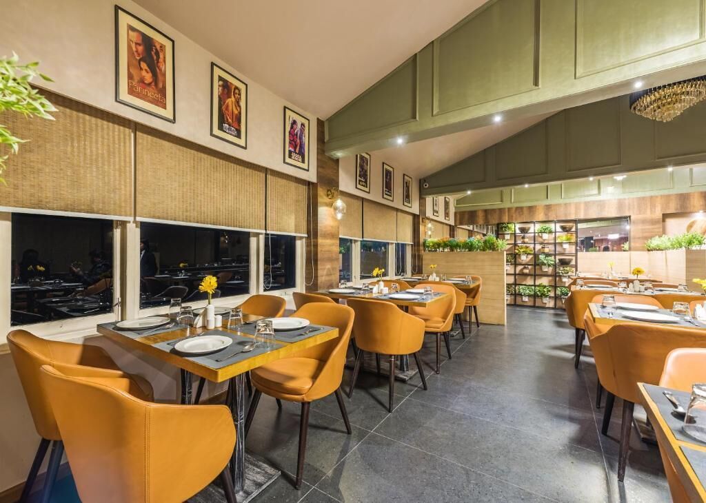 A restaurant with yellow chairs, tables set with plates and glasses, and framed pictures on the walls.