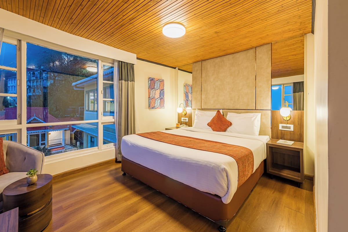 Hotelkamer met een groot bed, houten plafond, uitzicht op een gebouw en een kleine tafel met een plant.