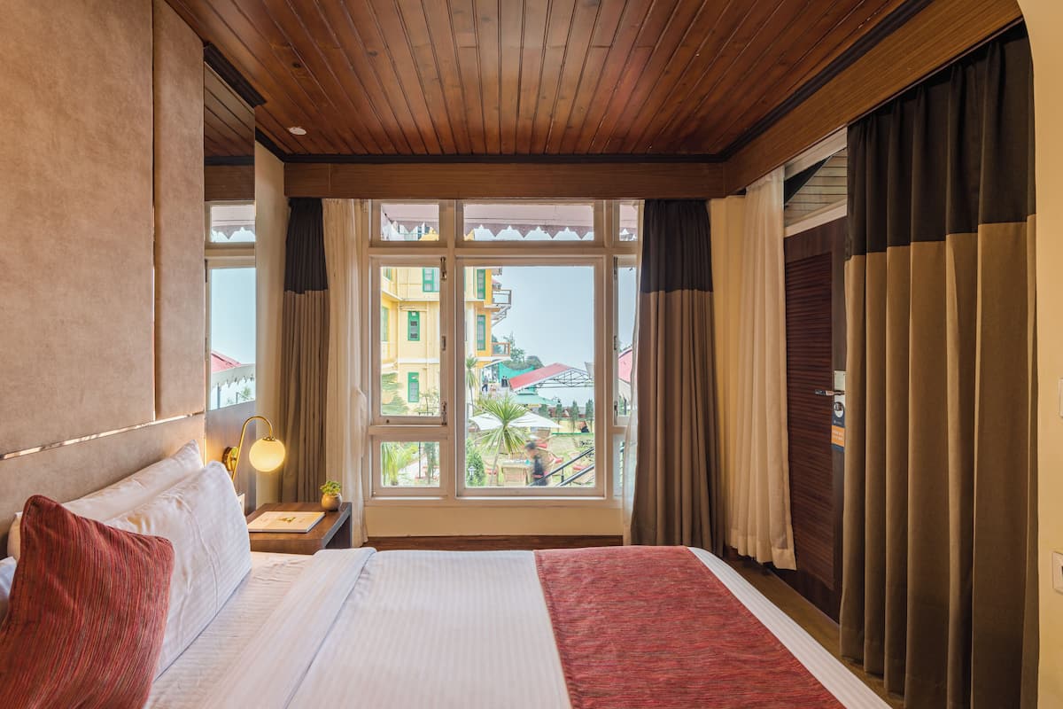 Een hotelkamer met een groot bed, houten plafond en uitzicht op gebouwen.