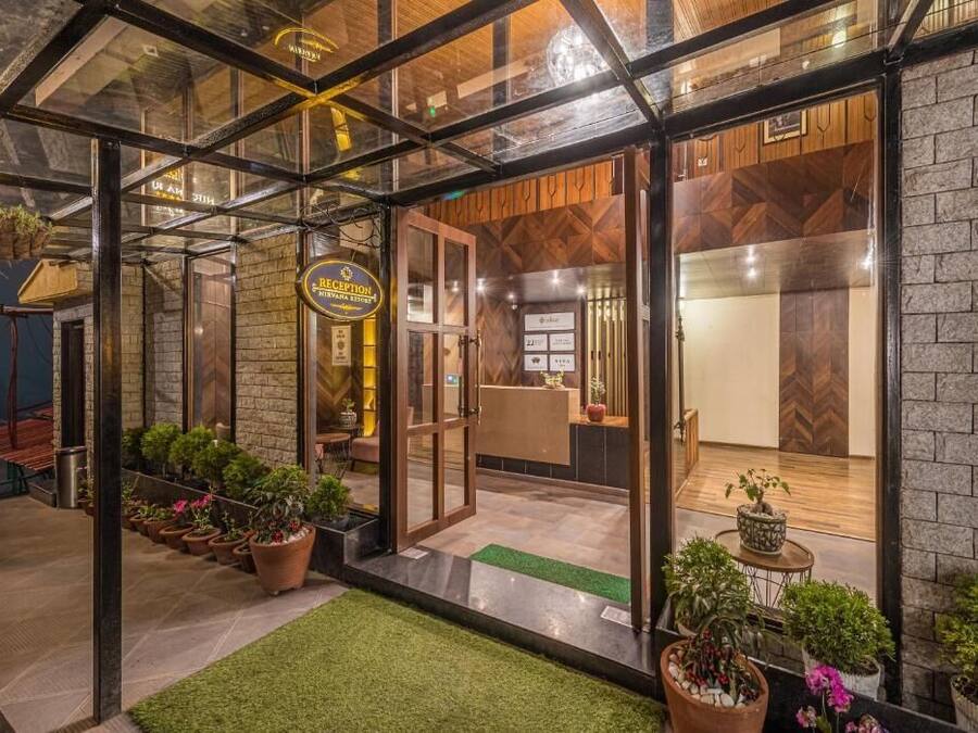 Zona de recepción con mostrador de madera, puertas de cristal y plantas en macetas.