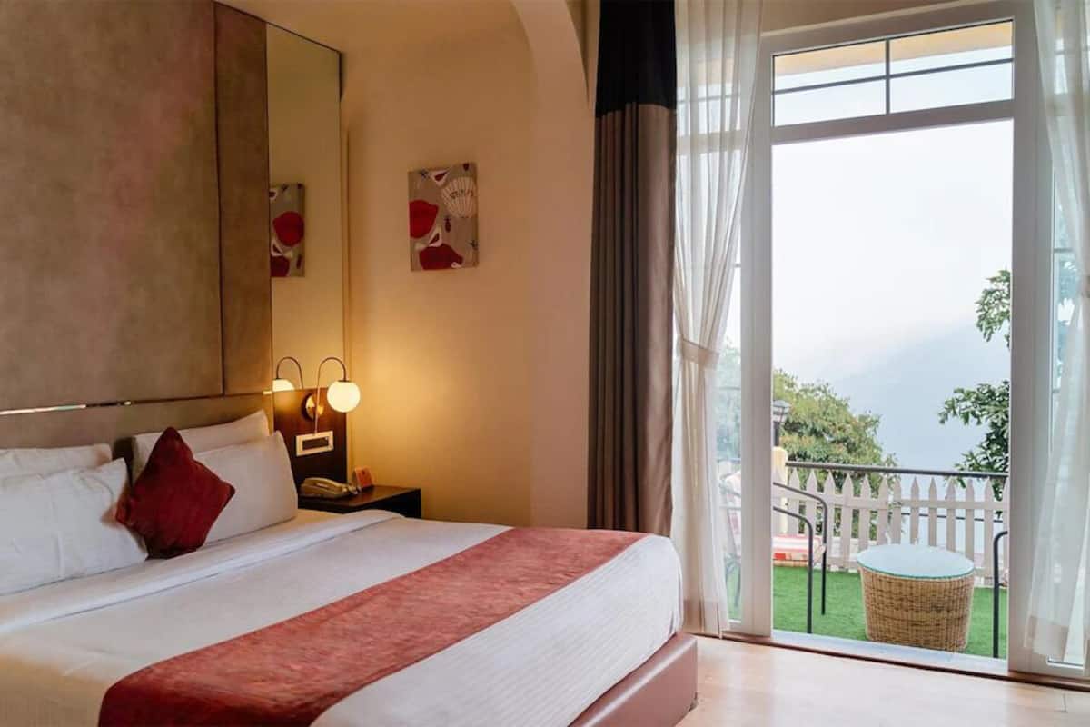 Een hotelkamer met een groot bed, een nachtkastje met een lamp, en uitzicht op een balkon met buitenmeubilair.