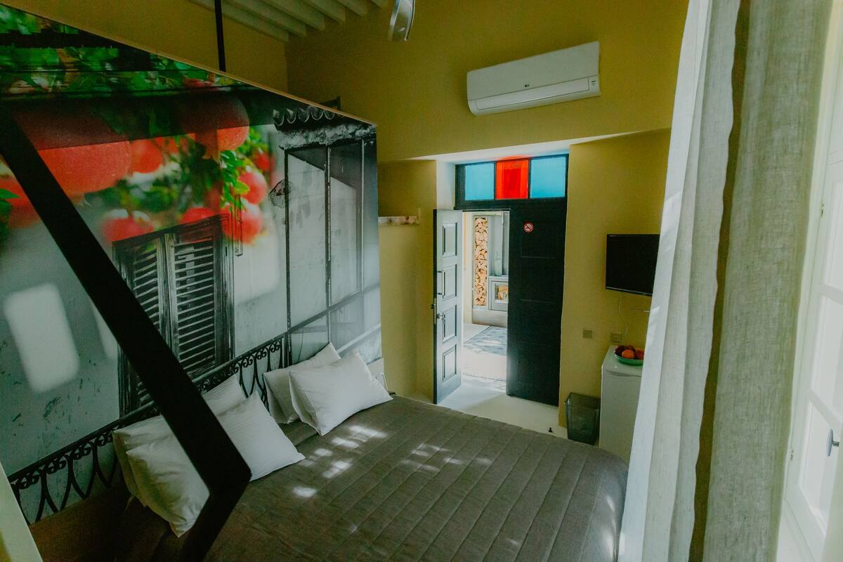 A bedroom with a bed, a TV, and a door leading to a bathroom.