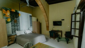 A bedroom with a bed, a desk, a TV, and a dining table with fruit. - Casa Mespilea Guest House (Paphos)
