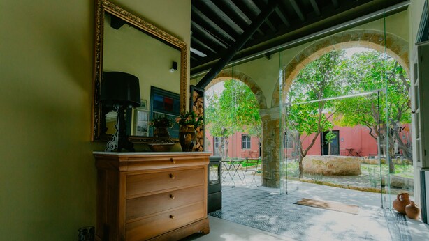 A room with a wooden dresser, a mirror, and a view of an outdoor courtyard with arches and trees. - Casa Mespilea Guest House (Paphos)