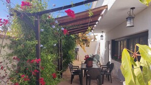 Eine Außenpatio mit einer Pergola, die mit blühenden Pflanzen bewachsen ist, einem Tisch mit Stühlen und einem hängenden Laternen.