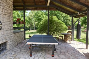 A covered outdoor area with a table tennis table, stone flooring, a clock, and potted plants.