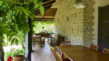 A covered patio with a stone wall, wooden furniture, and hanging plants.