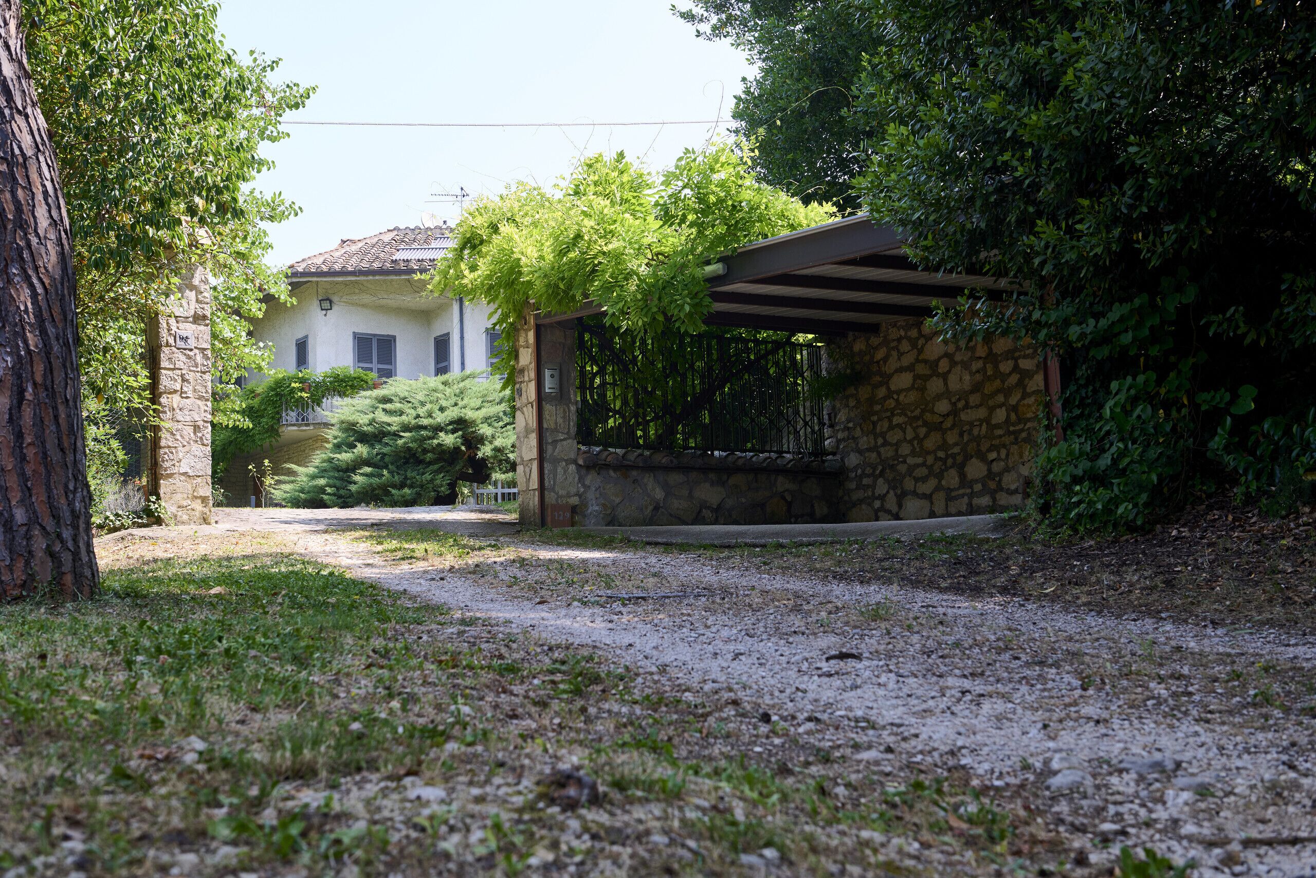 A gravel driveway leading to a stone building with a tiled roof, surrounded by greenery.