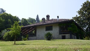 Een stenen huis met pannendak, een houten pergola en een gazon.