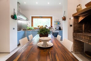 A modern kitchen with a wooden dining table, blue cabinets, and a brick fireplace.
