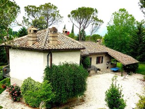 A rustic house with a tiled roof, a small attached structure with a sloped roof, and a gravel driveway.