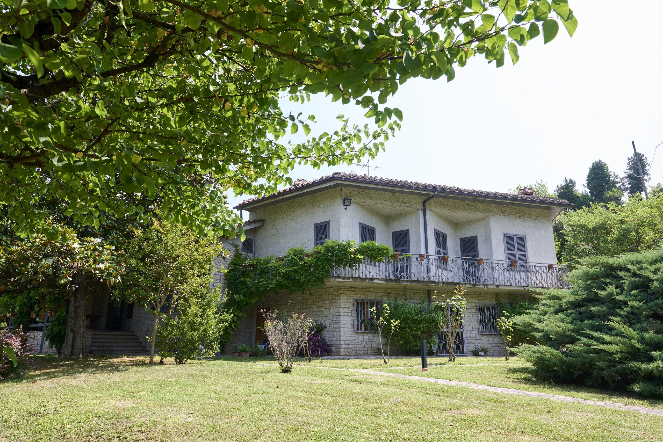 A two-story building with a balcony, surrounded by greenery.